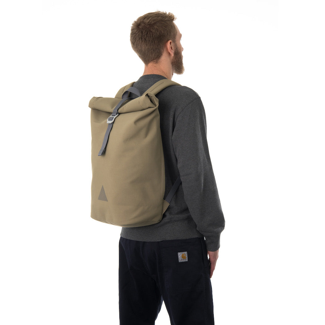 Man carrying khaki rolltop backpack.
