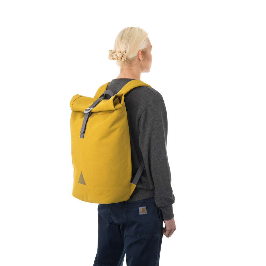 Woman carrying yellow rolltop backpack.